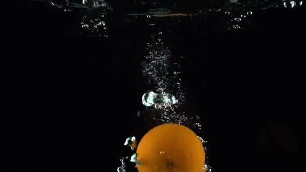 Whole orange sinks in water against black background super slow motion — Stok video