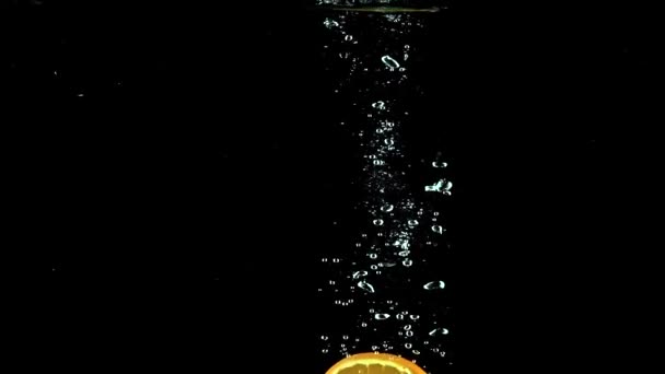 Naranja rebanada cae en el agua contra fondo negro video en cámara súper lenta — Vídeo de stock