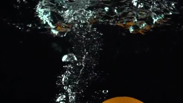 Érett narancs süllyed a víz sötét háttér szuper lassú ellen — Stock videók