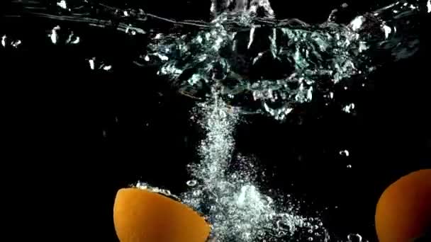 Закрыть супер замедленное видео, где апельсин расщепляется пополам и тонет в воде — стоковое видео