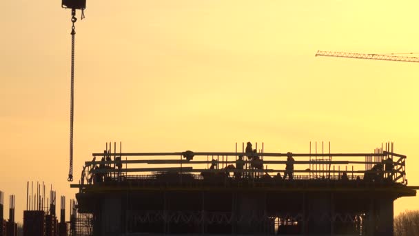 Siluetas de los trabajadores de la construcción contra el cielo naranja. Lente de teleobjetivo 4K — Vídeos de Stock