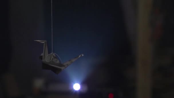 Papper origami crane hänger på tråden mot starkt ljus av projektor — Stockvideo