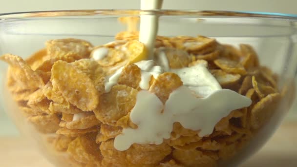 Verter un poco de leche sobre hojuelas de maíz dorado en un tazón de vidrio video en cámara súper lenta — Vídeos de Stock