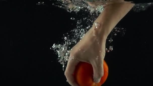 Человек протягивает руку и хватает томат, плавающий под водой, супер медленный выстрел. — стоковое видео