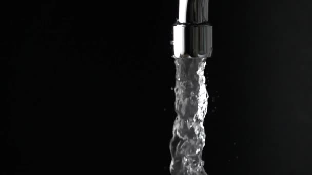 Close up slow motion shot of water running from tap against black background — Stok Video
