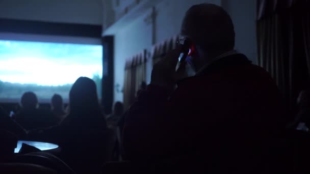 Man praten op zijn mobiele telefoon in donkere bioscoop zaal-reglementen overtreedt — Stockvideo