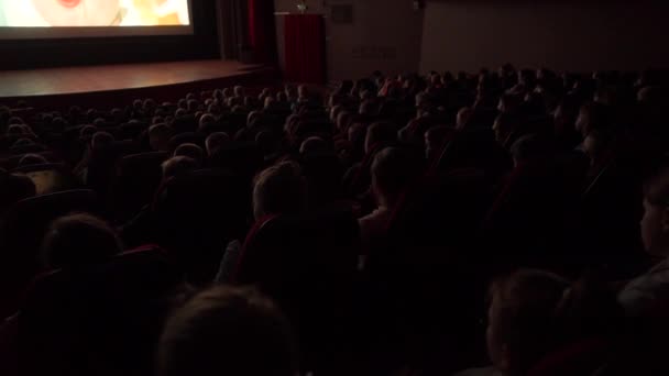 Beaucoup d'enfants regardent des films de dessins animés dans une grande salle de cinéma sombre — Video