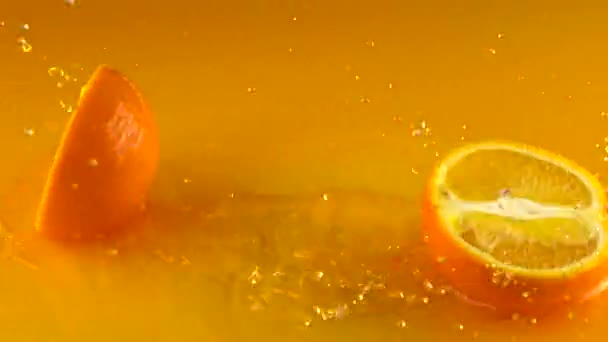 Orange hits orange juice surface and splits into halves. Slow motion video — Stock Video