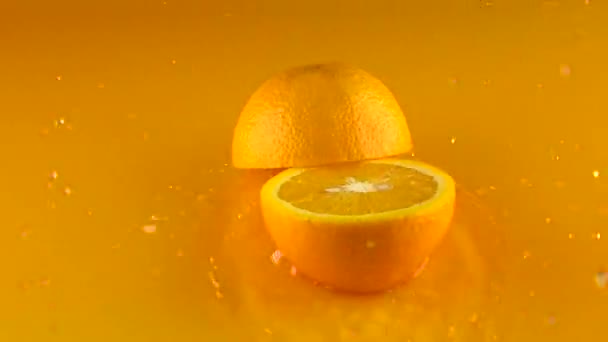 La naranja golpea la superficie del jugo de naranja y se divide en mitades. Vídeo en cámara lenta — Vídeo de stock