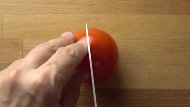 Чоловік розщеплює цілий червоний помідор на дерев'яній обробній дошці. 4K крупним планом відео — стокове відео