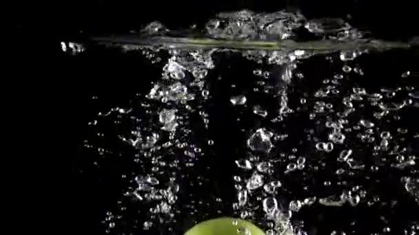 Zeleného jablka padají ve vodě proti černému pozadí, super slow motion — Stock video