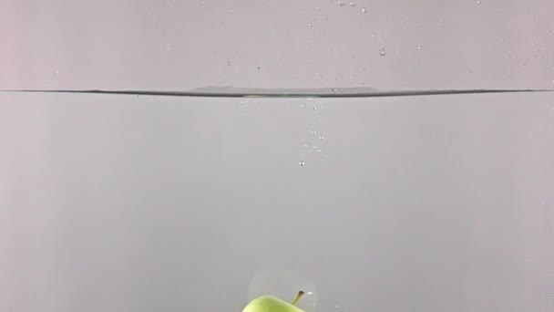 Groene appel vallen in water tegen grijze achtergrond, Super Slow Motion — Stockvideo