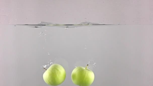 Dos manzanas verdes caen en el agua sobre fondo gris, super cámara lenta — Vídeo de stock