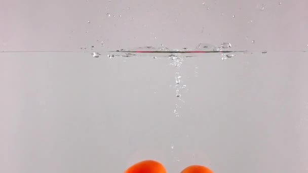 High speed camera video: red ripe tomatoes splash in water, grey background — Stock Video