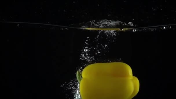 Sweet yellow pepper falls down in water, black background super slow motion shot — Stock Video