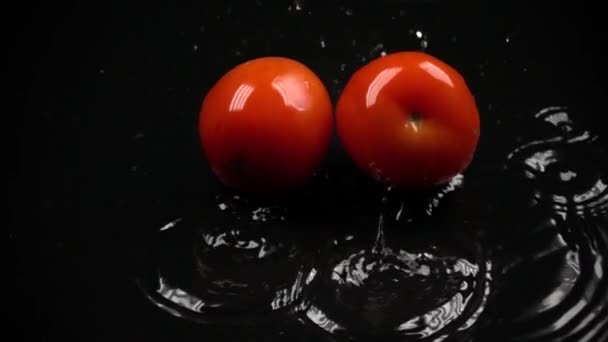 Super cámara lenta de dos tomates rojos maduros golpeando la superficie húmeda oscura — Vídeo de stock