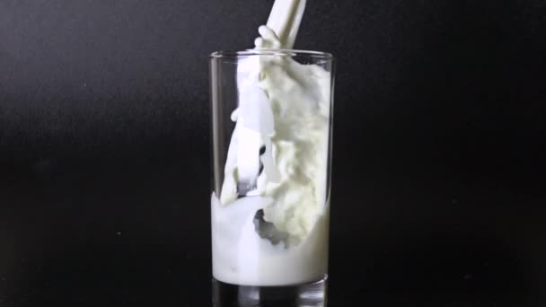 Gieten melk in glazen tegen zwarte achtergrond. 500 fps super slowmotion video — Stockvideo