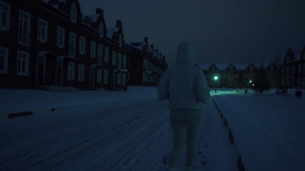 Solitario giovane donna in giacca d'argento a piedi sulla neve in zona residenziale di notte — Video Stock