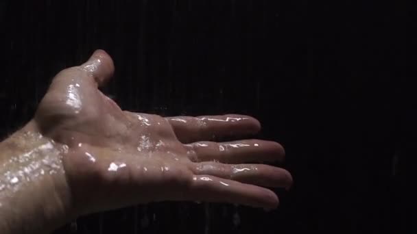 Ręką człowieka pod prysznicem z czarnym tłem, film w zwolnionym tempie — Wideo stockowe