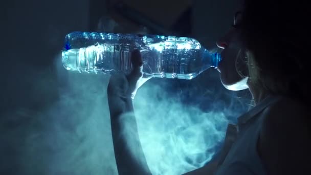 Het drinkwater van de meisje uit de plastic fles. Weinig licht video met rokerige achtergrond — Stockvideo