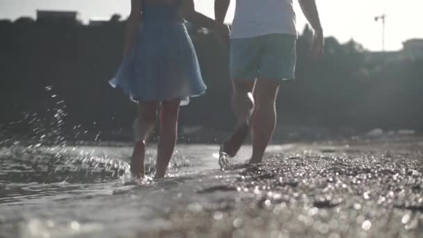 Een man in korte broek en een meisje in jurk wandelen op het strand — Stockvideo