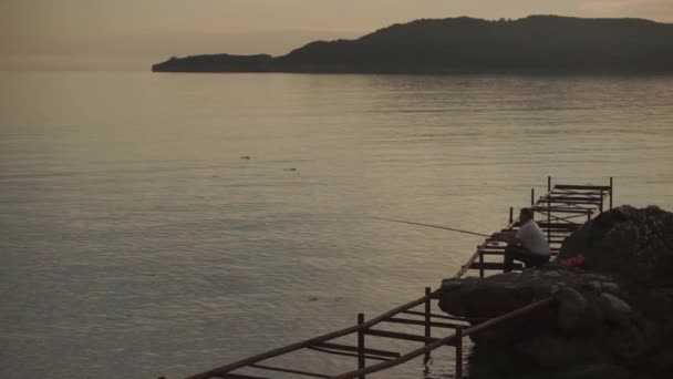 Pescador lança uma vara de pesca no mar sentado no banco à noite — Vídeo de Stock