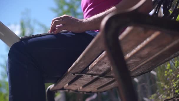 Hombre sentado en un banco con un portátil, y luego saldrá al aire libre — Vídeo de stock