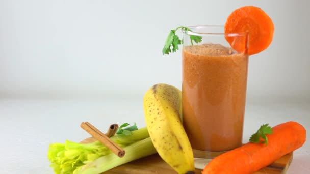 Narancssárga smoothy egy pohár. Banán, sárgarépa, petrezselyem és zeller. 4k dolly videóinak — Stock videók