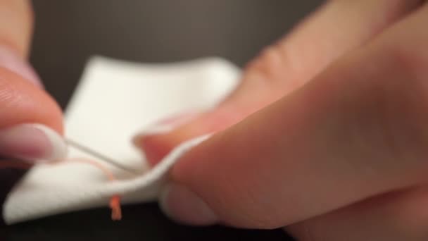 Hermosas manos femeninas cosiendo un paño blanco con un hilo naranja — Vídeos de Stock