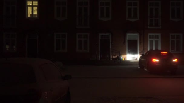 Big car drives away from a red brick townhouse at night — Stock Video