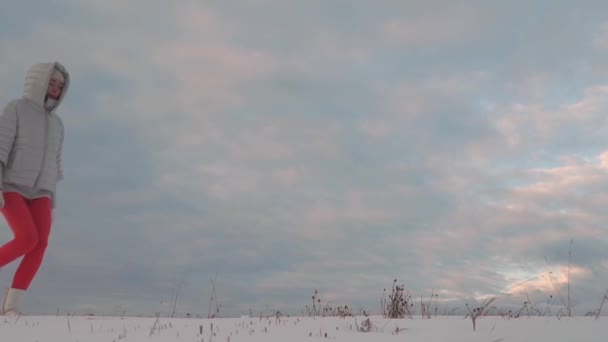 Young woman in silver jacket and red breeches walking on snow against cloudy sky — Stockvideo