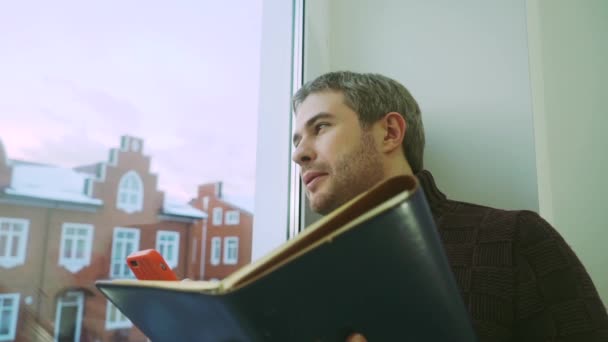 Bonito homem de camisola verificando seu planejador e falando ao telefone — Vídeo de Stock