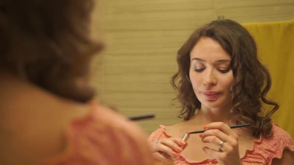 Hermosa chica en un vestido rosa poniendo un lápiz labial en sus labios por el espejo — Vídeos de Stock