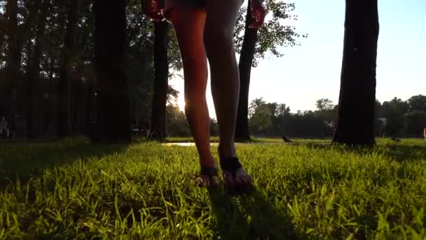 Slow motion steadicam shot de fille en sandales marchant dans le parc de coucher de soleil d'été — Video