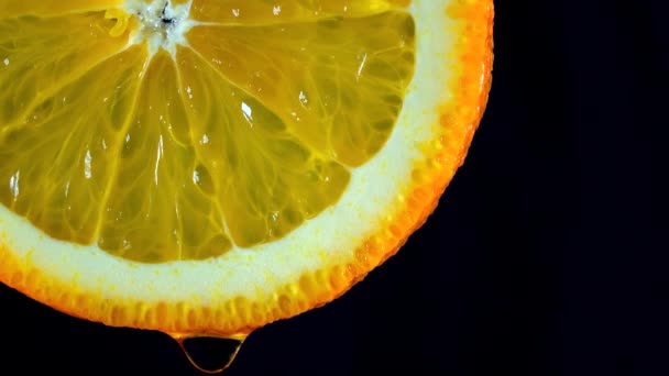 Macro 4K video de naranja rebanada y goteo de agua sobre fondo negro — Vídeo de stock