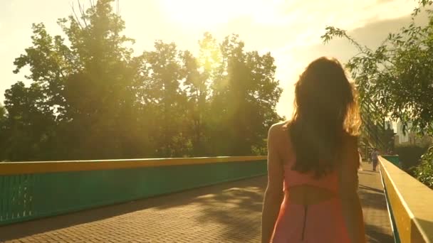 Slim μελαχρινή κοπέλα σε ροζ φόρεμα βόλτες στη γέφυρα. Αργή κίνηση steadicam κλιπ — Αρχείο Βίντεο
