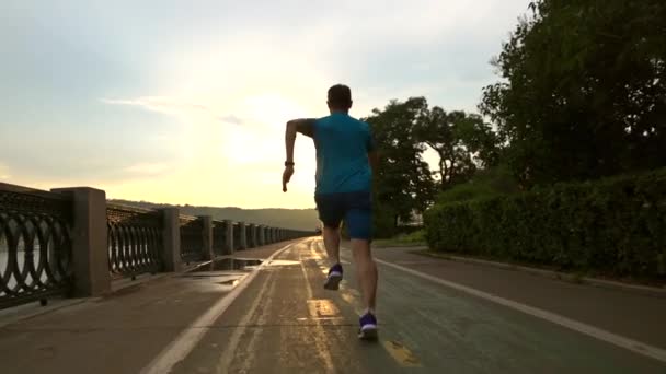 Runner in blauwe kleren lopen van de camera langs de zomer zonsondergang dijk van Moskou rivier. Slow Motion Steadicam geschoten op 120 fps — Stockvideo