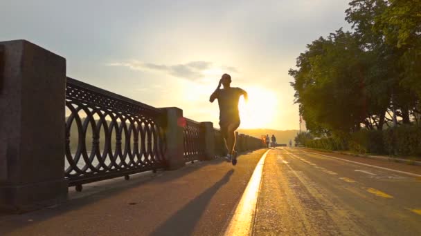 Sportler in blauer Uniform, der auf dem sommerlichen Sonnenuntergangdamm entlang der Fahrradstraße in Moskau läuft. Super Zeitlupe Steadicam aufgenommen mit 240 fps — Stockvideo