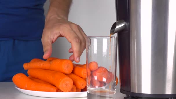 Man in blue clothes making carrot juice with shiny juicing machine. 4K shot — Stock Video