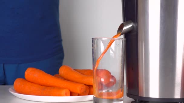 Homem de roupas azuis fazendo suco de cenoura com espremedor polido. 4K tiro — Vídeo de Stock