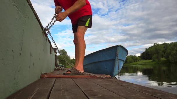 Unrecognizable man in a red t-shirt unties a boat at the pier. Slow motion shot — Stock Video