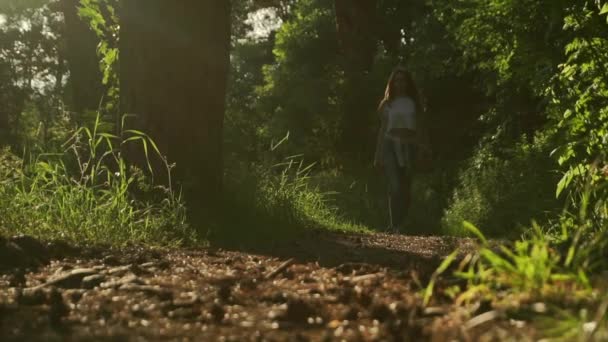 Chica morena caminando hacia la cámara en el bosque de coníferas puesta de sol. Tiro medio estático en cámara lenta — Vídeo de stock