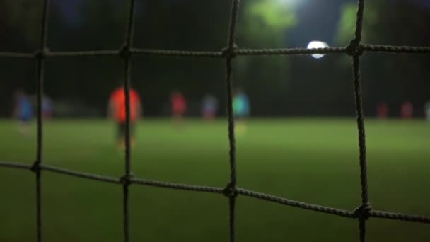 Juego de fútbol nocturno en cámara lenta video bokeh. Vista a través de malla — Vídeos de Stock