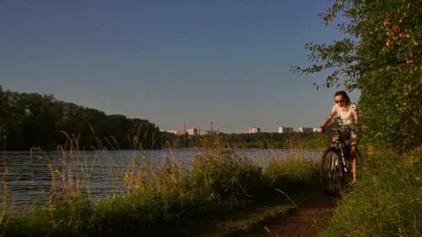 Piękna Brunetka Dziewczyna jazda na rowerze wzdłuż latem nad rzeką. Slow motion shot — Wideo stockowe