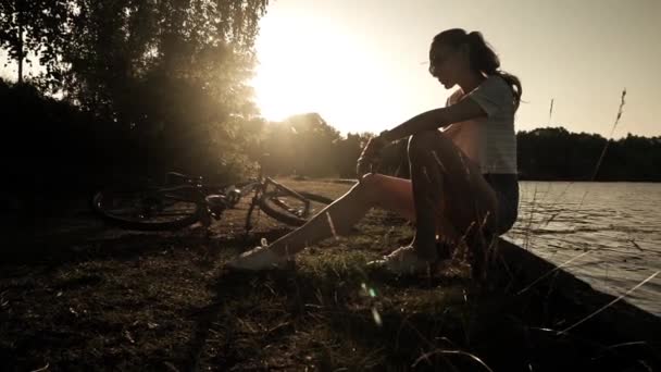 Štíhlá dívka cyklista s culíkem účes oddechuje. Zpomalený záběr proti západu slunce — Stock video