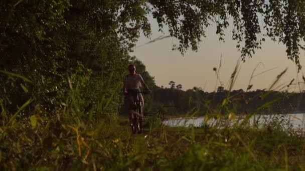 Струнка брюнетка дівчина катається на велосипеді вздовж літнього узбережжя річки. Повільний постріл — стокове відео