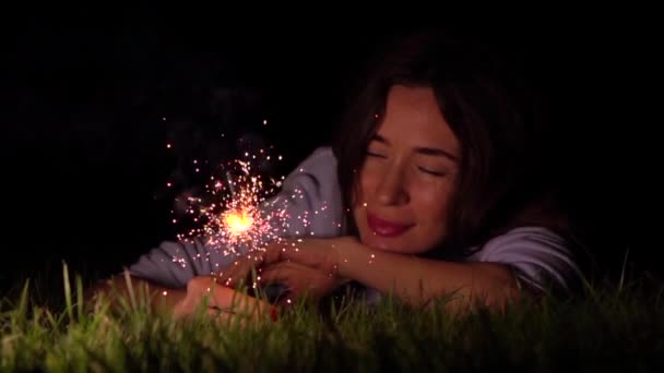 Romantic thoughtful girl laying on the grass with burning sparkler at night. Super slow motion video shot at 500 fps — Stock Video