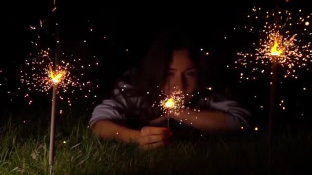 Wanita muda yang termenung di rumput dengan kembang api yang menyala di malam hari. Video gerak super lambat ditembakkan pada 500 fps — Stok Video