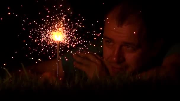 Einsamer Mann mittleren Alters, der nachts mit brennender Wunderkerze im Gras liegt, aus nächster Nähe. Super Zeitlupe Video aufgenommen bei 500 fps — Stockvideo