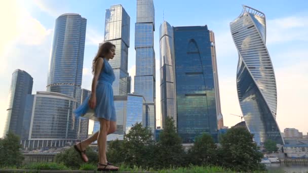 Тонкий дівчина в блакитному платті ходити проти сучасних хмарочоси, супер повільний рух відео, 250 кадрів в секунду — стокове відео